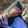 A woman at the beach wearing three Rosecliff rings and a Terra Newport Bracelet featuring 4mm sapphire and emerald gemstones.