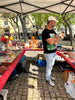 A man standing at flea market stall outside featuring assorted jewelry pieces and trinkets.