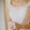 Close-up of a bride wearing a scoop neck wedding dress featuring detailed lace filigree. 