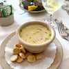 A bowl filled with chowder sits on a plate with oyster crackers.