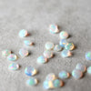 Loose 4mm briolette cut sustainably grown opals scattered across a gray background.