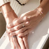 Woman's hands covered with rings, including a 14k gold Rosecliff Letter Ring, showcasing alternating 2 mm faceted round cut, prong set Pink Sapphires and Diamonds.