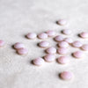 Loose 6mm briolette cut, sustainably grown pink opals scattered across a white background.
