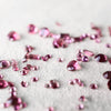 Scattered assortment of loose pink tourmaline gemstones of various cuts and sizes on a white fabric background.