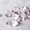 Scattered assortment of 8x10mm emerald cut, loose rose quartz gemstones on a white fabric background.