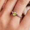 Woman's finger adorned with a 14k gold Rosecliff Grand Ring with a 6 mm round, briolette-cut Peridot and eight 2 mm round-cut Diamonds.