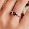 Woman's finger adorned with a 14k gold Rosecliff Grand Ring with a 6 mm round, briolette-cut Garnet and eight 2 mm round-cut Diamonds.