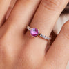 Woman's finger adorned with a 14k gold Rosecliff Grand Ring with a 6 mm round, briolette-cut Pink Sapphire and eight 2 mm round-cut Diamonds.