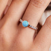 Woman's finger adorned with a 14k gold Rosecliff Grand Ring, featuring a 6 mm round, briolette-cut Turquoise and eight alternating 2 mm round-cut Diamonds and Nantucket Blue Topazes.