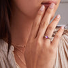 Woman's hand adorned with a 14k gold Rosecliff Grand Ring, featuring a 6 mm round, briolette-cut Pink Sapphire and eight alternating 2 mm round-cut Diamonds.