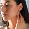 Woman wearing two Rosecliff huggie earrings including one featuring 2 mm round cut Nantucket blue topaz prong set in 14k gold