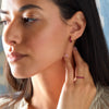 Woman wearing two Rosecliff huggie earrings including one featuring 2 mm round cut rubies prong set in 14k yellow gold