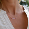 Woman wearing a Rosecliff bar necklace and huggie earrings featuring 2 mm round cut pink sapphires prong set in 14k gold