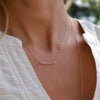 Woman wearing a Rosecliff bar necklace with eleven 2 mm faceted round cut pink sapphires prong set in solid 14k yellow gold