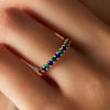 Close-up of a hand adorned with a 14k gold Terra Rosecliff Stackable Ring featuring alternating sapphires and emeralds.