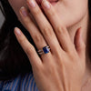 Woman wearing a Warren ring in 14k gold with accent diamonds featuring one 10 x 8 mm emerald cut bezel set sapphire