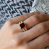 Woman's hand showcasing a 14k yellow gold Warren Vertical Garnet Ring with accent diamonds featuring one 10 x 8 mm emerald cut bezel set garnet.