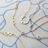 Flat Horseshoe necklace with Adelaide Mini chain, Small Flat Horseshoe necklace, & two infinity necklaces in 14k yellow gold.