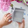 Toddler's hands holding a signature jewelry gift box wrapped with a satin ribbon.