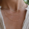 Woman wearing a layered Adelaide necklace, Adelaide Mini necklace, and Saffron necklace, all in 14k yellow gold.