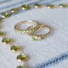 A Rosecliff ring gently lays on a Greenwich Solitaire ring with a Newport necklace in the background, all featuring peridot.