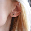 Woman wearing a Birthstone Stud Earring featuring a 4 mm briolette cut Garnet bezel set in 14k yellow gold