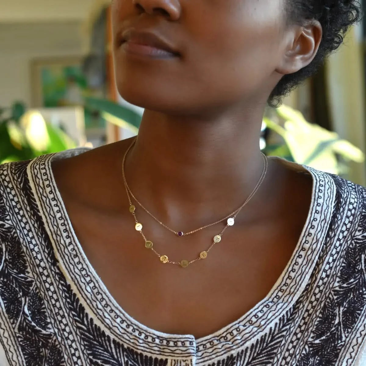 Woman wearing two necklaces including a 14k gold necklace featuring eight 1/4” flat engraved letter discs, spelling Fearless