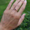 Hand wearing a 1.6 mm wide 14k yellow gold Grand ring featuring one 6 mm briolette cut bezel set garnet