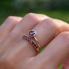 Hand wearing two rings including a 1.6 mm wide 14k yellow gold Grand ring featuring one 6 mm briolette cut bezel set garnet