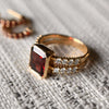 A 14k yellow gold Warren Vertical Garnet Ring with accent diamonds featuring one 10 x 8 mm emerald cut bezel set garnet