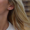 Woman wearing a 14k yellow gold Grand stud earring featuring one 6 mm briolette cut bezel set amethyst