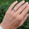 Hand wearing a 1.6 mm wide 14k yellow gold Grand ring featuring one 6 mm briolette cut bezel set pink sapphire