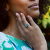 Woman with a Personalized Warren Horizontal Birthstone Ring with a stunning emerald-cut birthstone, set horizontally and accented with 16 prong-set gemstones in solid 14k gold