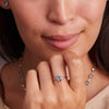 Woman's hand adorned with a stunning Nantucket Blue Topaz Grand Ring featuring a 6mm briolette-cut gemstone in a 14k gold bezel, perfect for stacking and December birthdays.