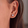 Woman showcasing a 14k yellow gold Grand stud earring featuring one 6 mm briolette cut bezel set moonstone