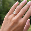 Hand wearing a 1.6 mm wide 14k yellow gold Grand ring featuring one 6 mm briolette cut bezel set moonstone