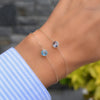 Woman wearing two Grand 1 Birthstone bracelets, each on a 1.17mm cable chain featuring aquamarine and Nantucket blue topaz.