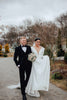 A groom stands to the left of the bride as they happily walk down a winter garden path.