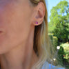 Woman wearing a pair of 14k gold Grand stud earrings each featuring one 6 mm briolette cut Pink Sapphire