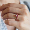 Hand wearing two rings: a Rosecliff Ruby Stackable Ring with 2mm Rubies and a 14k gold ring with a single bezel-set Ruby.