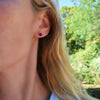 Woman wearing a pair of 14k yellow gold Grand stud earrings each featuring one 6 mm briolette cut Ruby