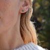 Woman wearing a Birthstone Stud Earring featuring a 4 mm briolette cut Emerald bezel set in 14k white gold