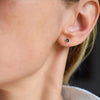 Woman wearing a Birthstone Stud Earring featuring a 4 mm briolette cut Emerald bezel set in 14k yellow gold