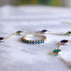 Assorted jewelry featuring a 14k gold Terra Rosecliff Stackable Ring with alternating sapphires and emeralds, surrounded by matching gemstone bracelets.