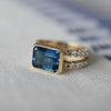 Aspect view of a Warren Horizontal Atlantic Blue Topaz Ring with Diamonds, featuring an 8 x 10mm Atlantic Blue Topaz and 16 prong-set diamonds in 14k yellow gold.