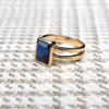 The Warren ring, crafted in 14k yellow gold, features a vertically placed, bezel-set emerald-cut sapphire measuring 10 x 8 mm.