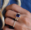 Woman's hand wearing a Rosecliff ring and a Warren ring in 14k gold with accent diamonds featuring one 10 x 8 mm sapphire