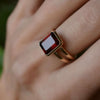 Hand with a Warren ring in 14k yellow gold featuring one 10 x 8 mm emerald cut bezel set garnet