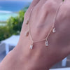 A woman's hand holding a Providence 5 Aquamarine drop necklace featuring 5 petite baguette cut stones set in 14k yellow gold