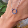 Hand holding a Rosecliff open circle necklace with sixteen 2 mm faceted round cut sapphires prong set in 14k yellow gold